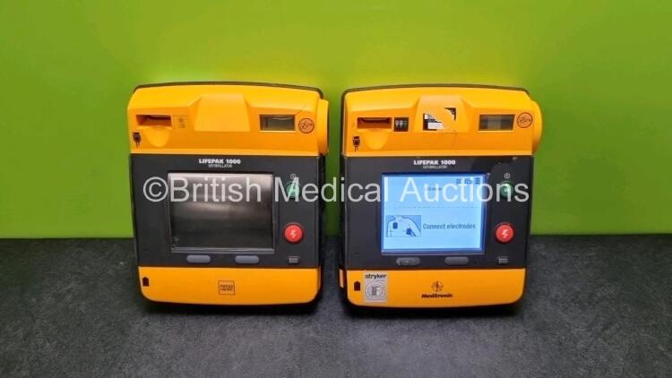 2 x Medtronic Physio Control Lifepak 1000 Defibrillators *Mfd 2016 / 2009* (Both Power Up with Stock Battery Stock Battery Not Included, Both with Damage to Casing - See Photo)