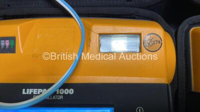 2 x Medtronic Physio Control Lifepak 1000 Defibrillators (Both Power Up with Cracks in Casing - See Photos ) with 2 x 3 Lead ECG Leads, 4 x Electrode Packs (All in Date) and 2 x Batteries *Install Before 2024 / 2024* - 4