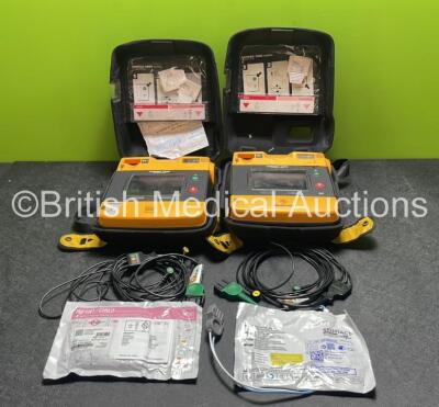 2 x Medtronic Physio Control Lifepak 1000 Defibrillators (Both Power Up with Cracks In Casing - See Photos) with 2 x ECG Leads, 2 x Electrode Packs (1 in Date, 1 Expired) and 2 x Batteries *Install Before 2025 / 2024* in Carry Cases