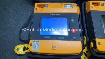 2 x Medtronic Physio Control Lifepak 1000 Defibrillators (Both Power Up with Cracks In Casing - See Photos) with 2 x ECG Leads, 2 x Electrode Packs (1 in Date, 1 Expired) and 2 x Batteries *Install Before 2025 / 2024* in Carry Cases - 4