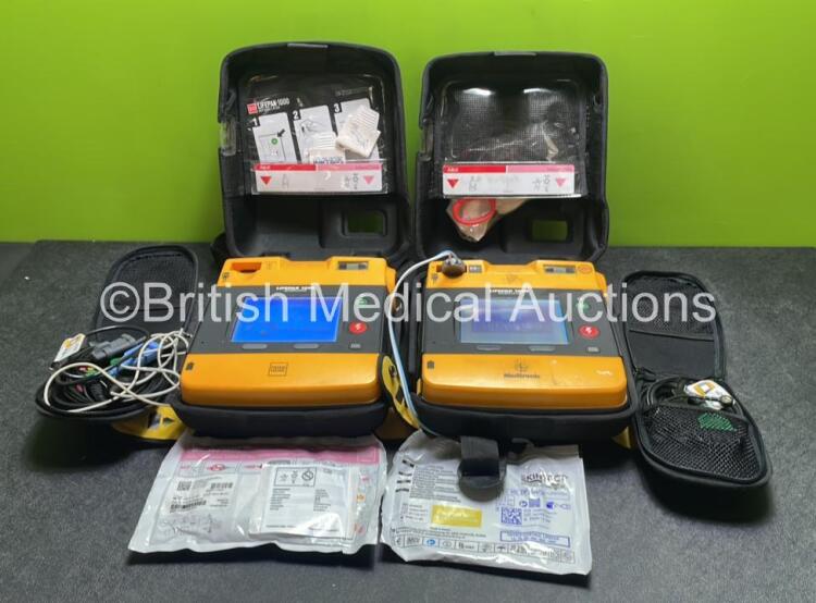 2 x Medtronic Physio Control Lifepak 1000 Defibrillators (Both Power Up with Cracks In Casing - See Photos) with 2 x ECG Leads, 2 x Electrode Packs (Both In Date) and 2 x Batteries *Install Before 2023 / 2024* in Carry Cases