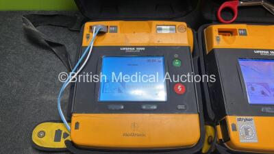 2 x Medtronic Physio Control Lifepak 1000 Defibrillators (Both Power Up with Cracks In Casing - See Photos) with 2 x Electrode Packs (Both In Date) and 2 x Batteries *Install Before 2025 / 2026* in Carry Cases - 4